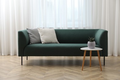 Stylish living room interior with comfortable green sofa and beautiful plant near window