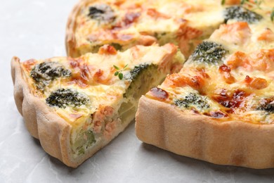 Photo of Delicious homemade quiche with salmon and broccoli on light gray table, closeup