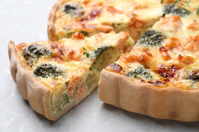 Delicious homemade quiche with salmon and broccoli on light gray table, closeup