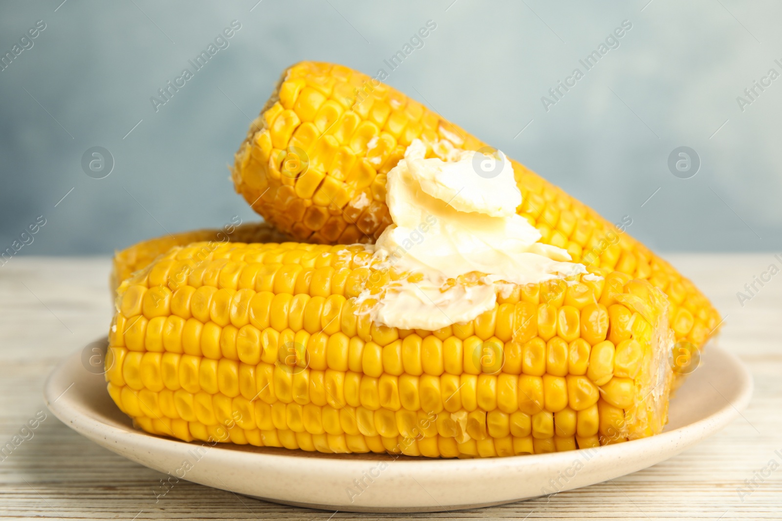 Photo of Delicious boiled corn with butter on white wooden table