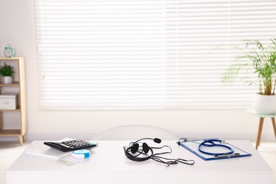 Photo of Headphones, calculator and medical items on white desk in clinic. Online doctor concept