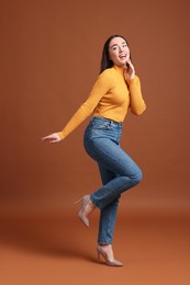Photo of Young woman in stylish jeans on brown background