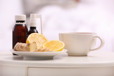 Photo of Cough syrups, lemon and cup of tea on table in bedroom