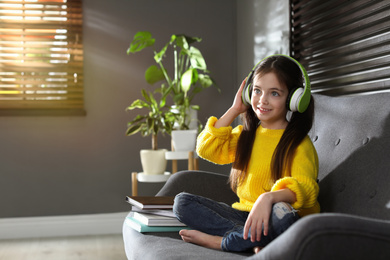 Cute little girl with headphones listening to audiobook at home