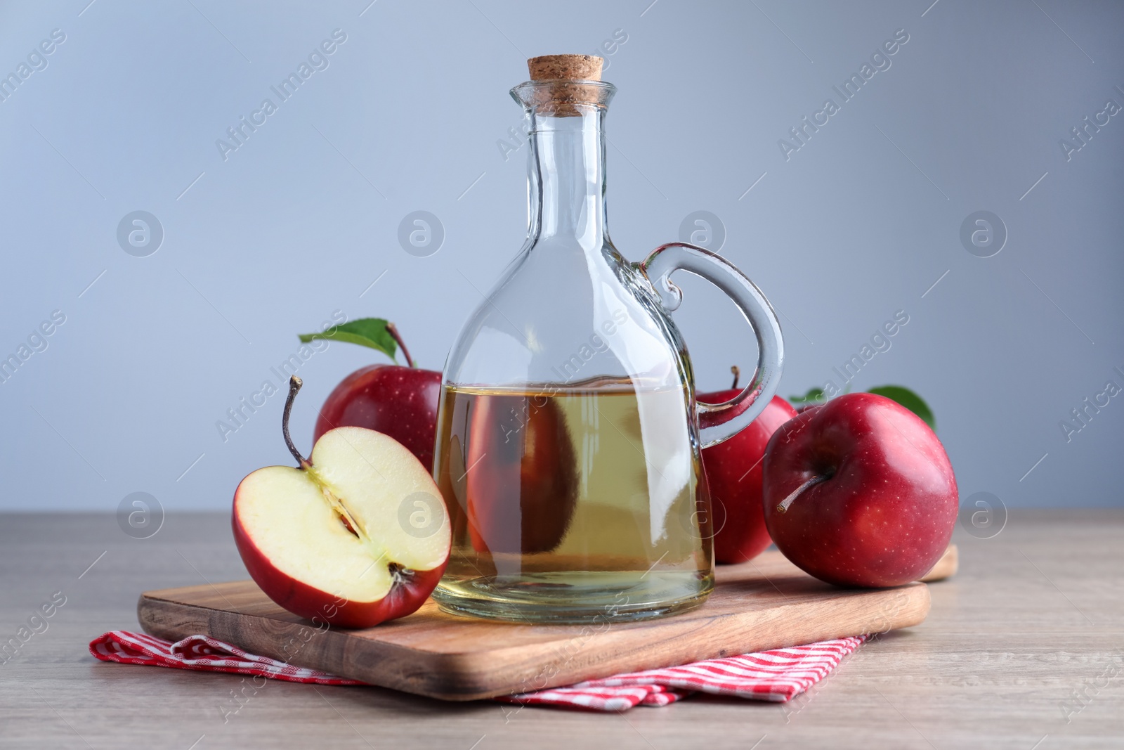 Photo of Jug of tasty juice and fresh ripe red apples on wooden table