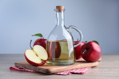 Photo of Jug of tasty juice and fresh ripe red apples on wooden table