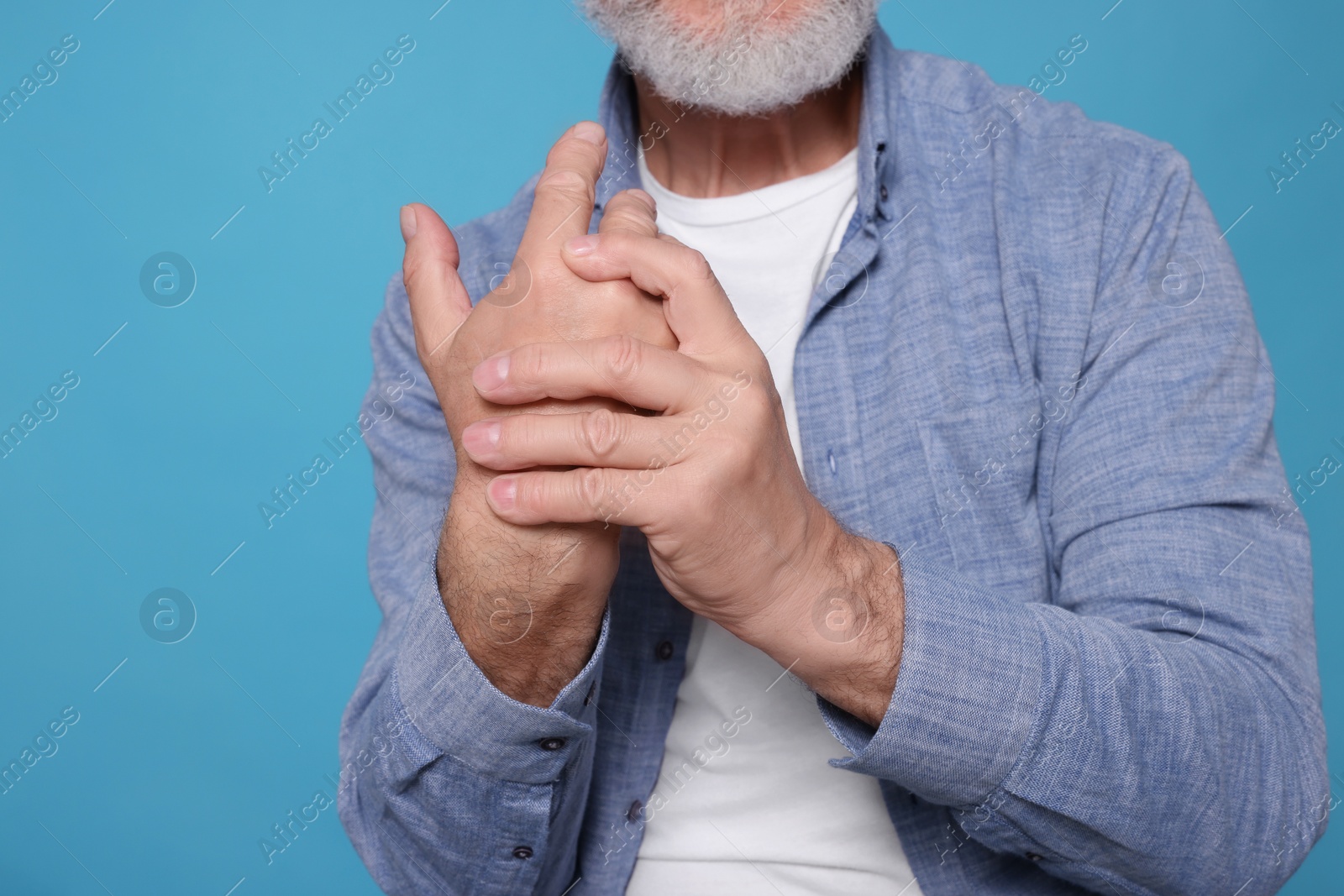 Photo of Senior man suffering from pain in hand on light blue, closeup. Arthritis symptoms