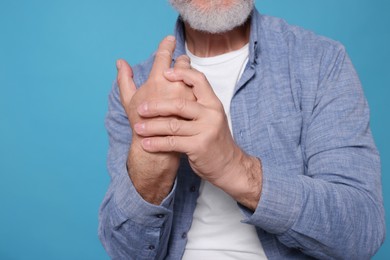 Senior man suffering from pain in hand on light blue, closeup. Arthritis symptoms