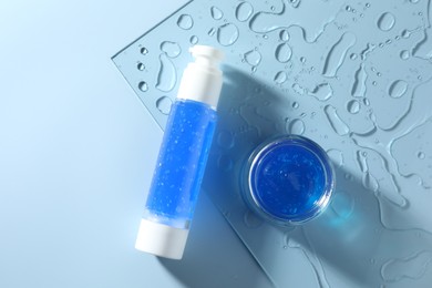 Bottle and jar of cosmetic products on light blue background, top view