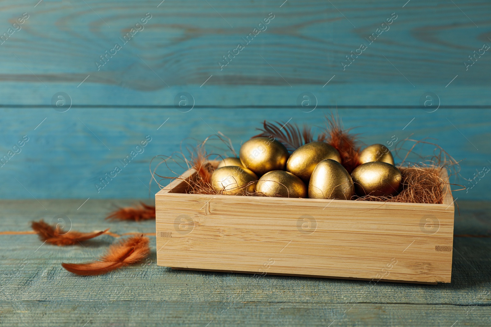 Photo of Crate with golden eggs on light blue wooden table