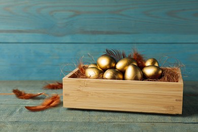 Crate with golden eggs on light blue wooden table