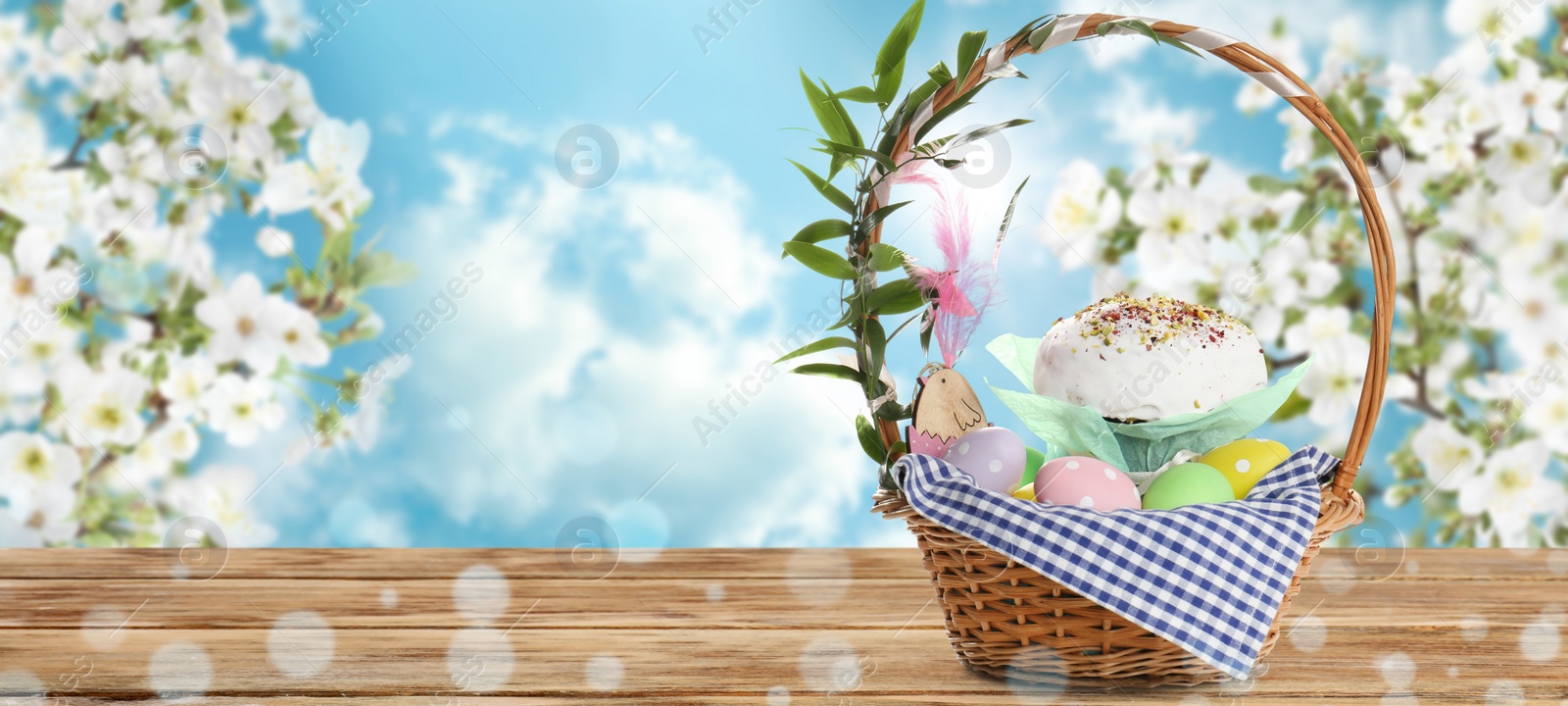 Image of Basket with traditional Easter cake and eggs on wooden table outdoors, space for text. Banner design