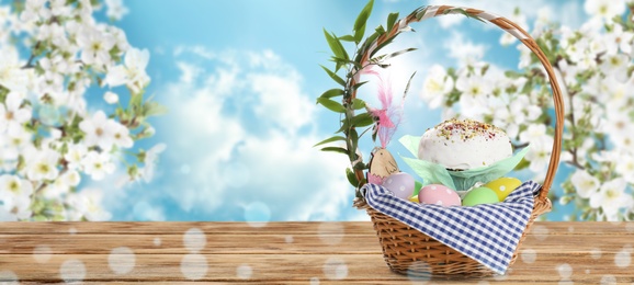Image of Basket with traditional Easter cake and eggs on wooden table outdoors, space for text. Banner design