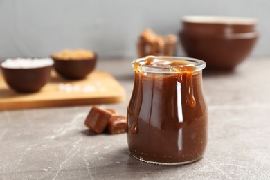 Jar with tasty caramel sauce on grey table. Space for text