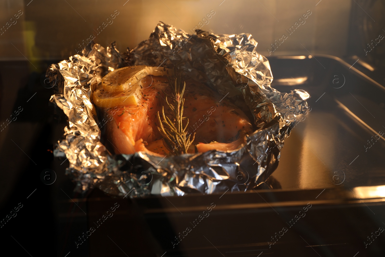 Photo of Foil with fish in oven, closeup. Baking salmon