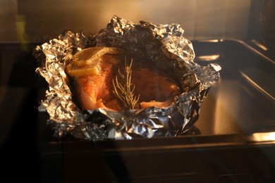 Photo of Foil with fish in oven, closeup. Baking salmon