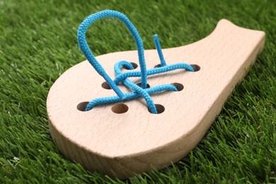 Photo of Wooden whale figure with holes and lace on artificial grass, closeup. Educational toy for motor skills development