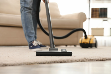 Photo of Young man using vacuum cleaner at home, closeup