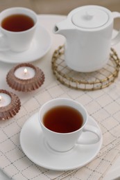 Cups of tea, teapot and burning candles on white table