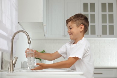 Photo of Boy filling glass with water from tap in kitchen