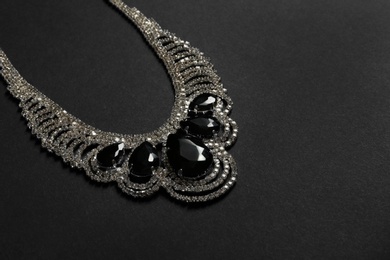 Stylish necklace with gemstones on black background, space for text. Luxury jewelry
