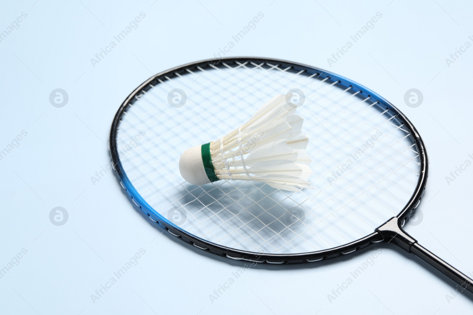 Photo of Feather badminton shuttlecock and racket on light blue background, closeup