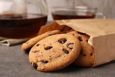 Photo of Paper bag with delicious chocolate chip cookies and tea on grey table, closeup