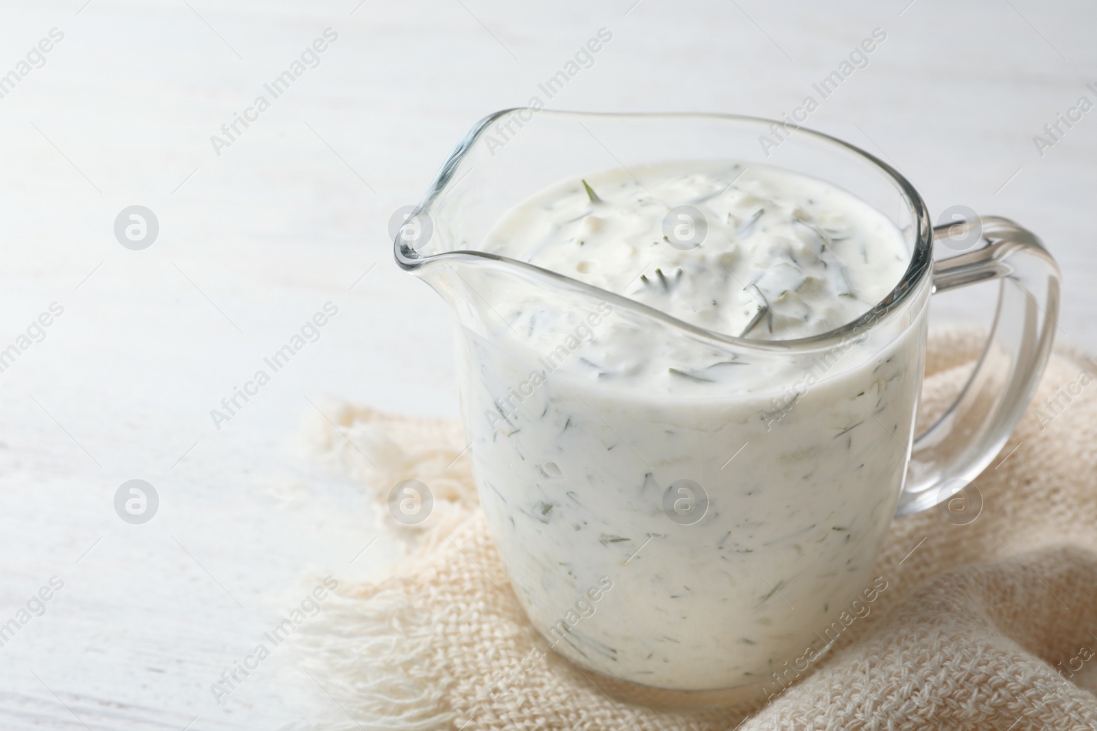 Photo of Glass jug of cucumber sauce on wooden background, space for text. Traditional Tzatziki