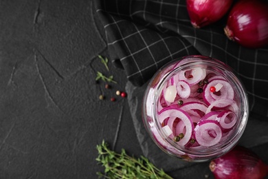 Flat lay composition with jar of tasty pickled onions on black table, space for text