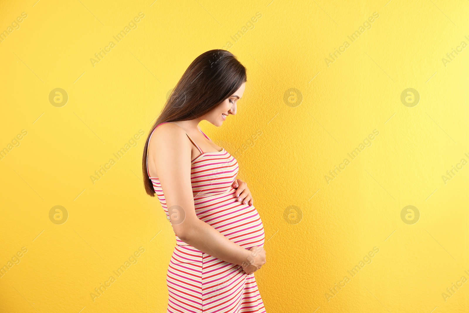 Photo of Beautiful pregnant woman holding hands on belly against color background