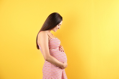 Beautiful pregnant woman holding hands on belly against color background