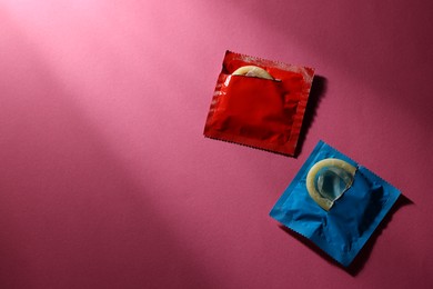 Photo of Condoms in torn packages on pink background, top view with space for text. Safe sex