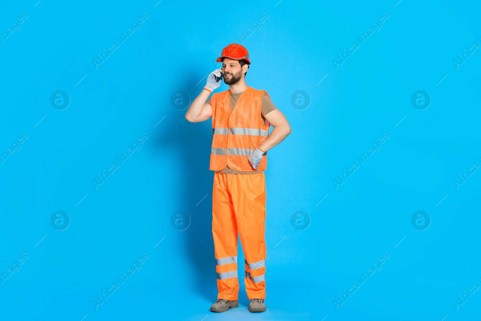 Photo of Man in reflective uniform talking on smartphone against light blue background