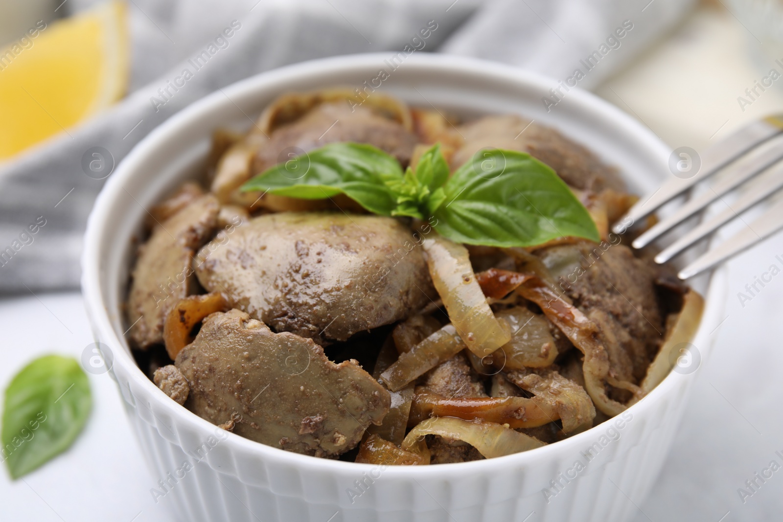 Photo of Delicious fried chicken liver with onion and basil in bowl on white table, closeup