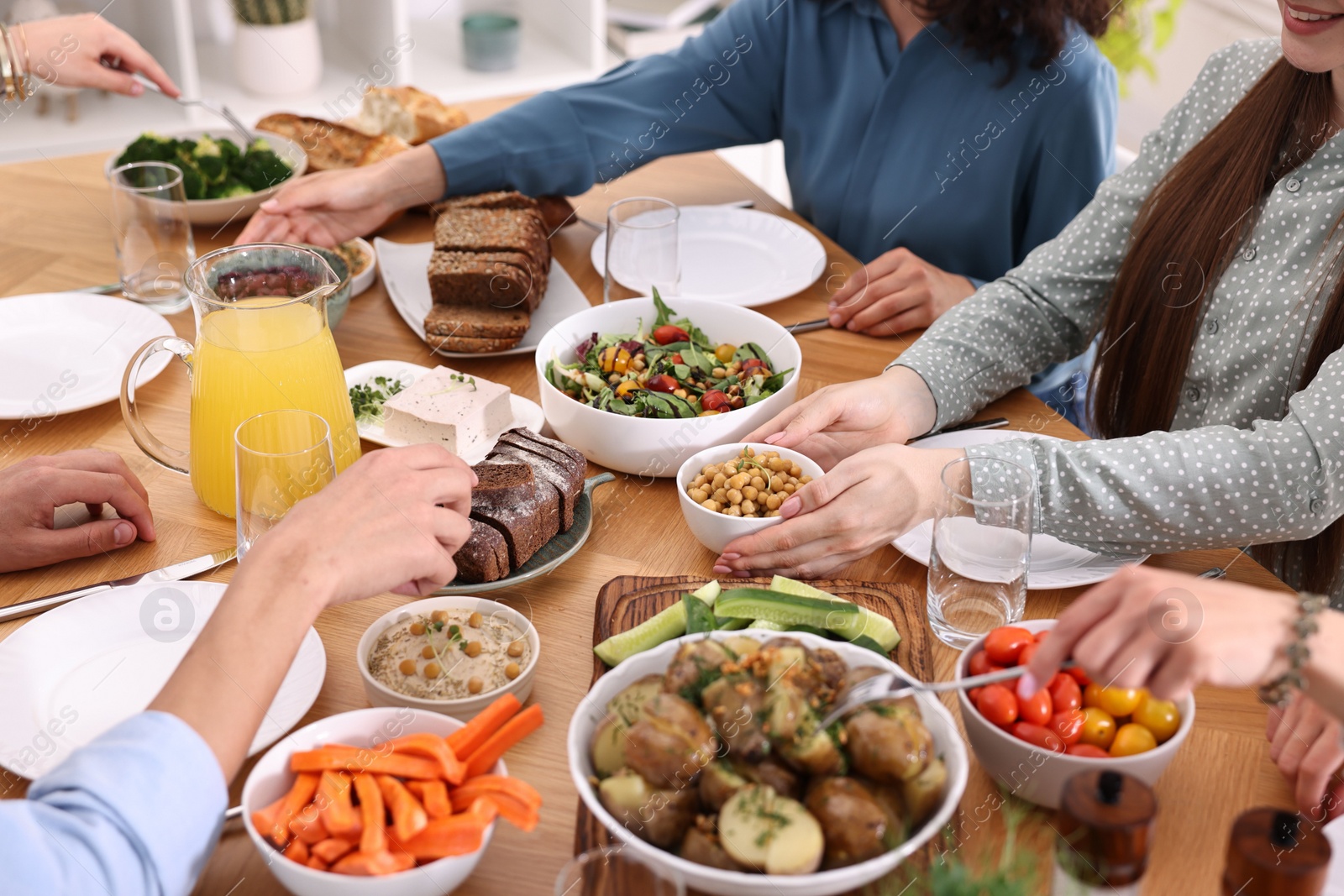 Photo of Friends eating vegetarian food at wooden table indoors, closeup