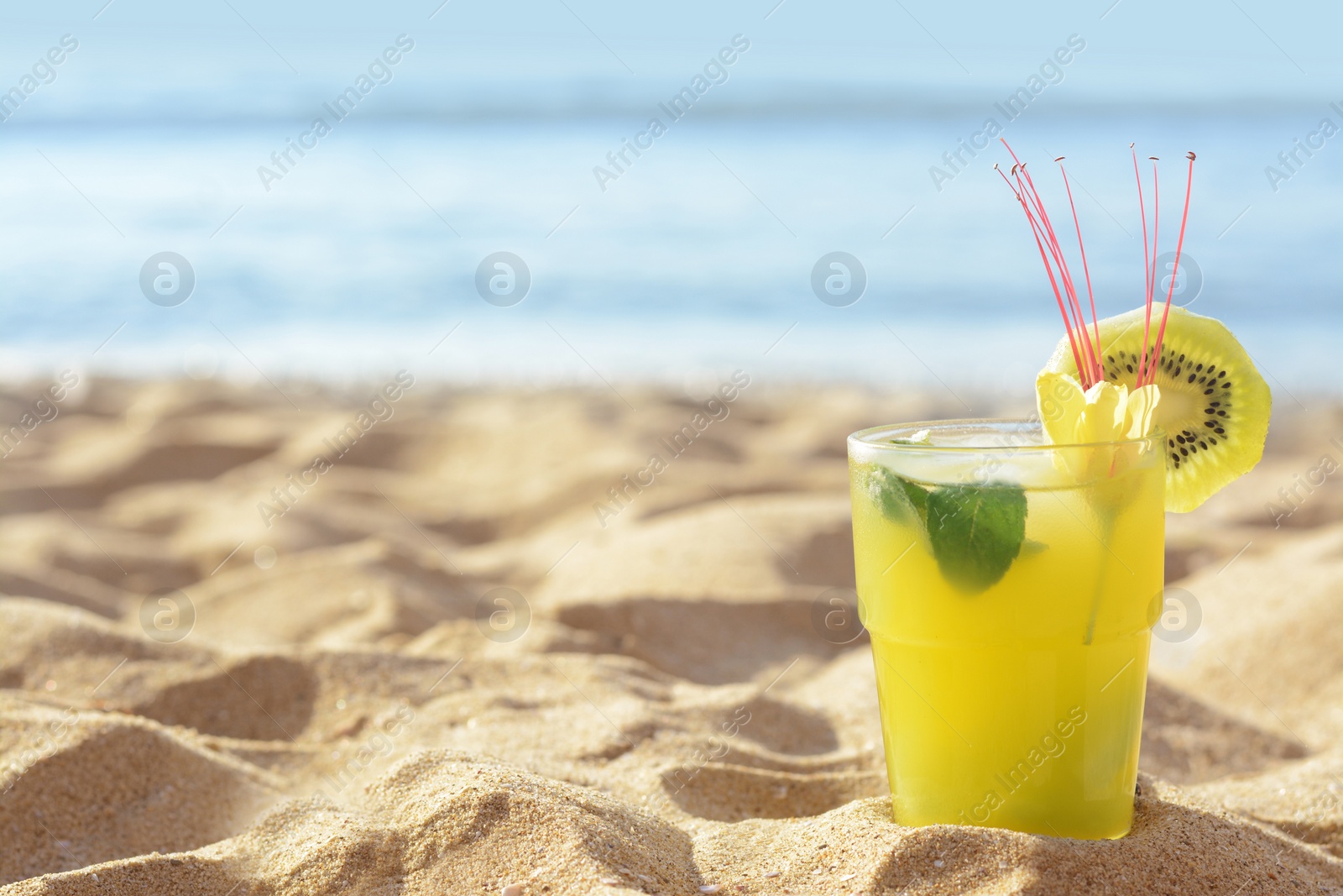 Glass of refreshing drink with kiwi and mint on sand near sea. Space for text Photo of Glass of refreshing drink with kiwi and mint on sand near sea. Space for text