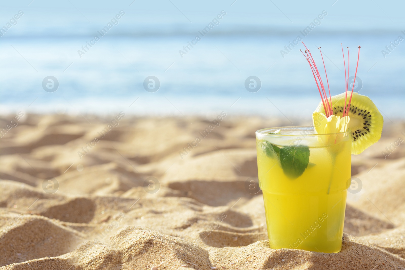 Photo of Glass of refreshing drink with kiwi and mint on sand near sea. Space for text