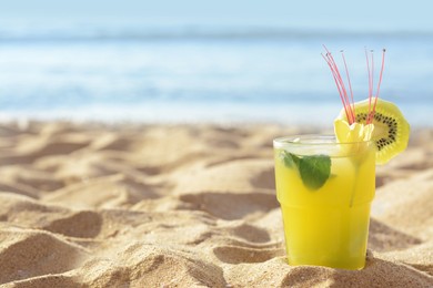 Photo of Glass of refreshing drink with kiwi and mint on sand near sea. Space for text