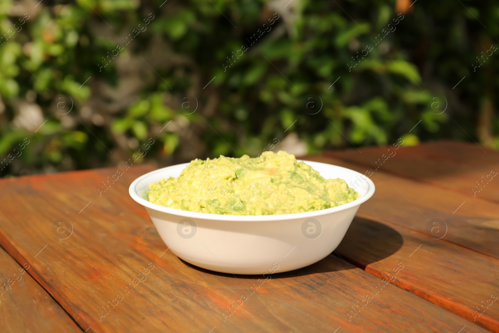 Photo of Delicious guacamole made of avocados on wooden table outdoors