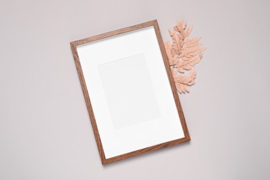 Photo of Empty photo frame and decorative leaf on light gray background, flat lay. Mockup for design