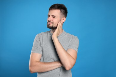 Young man suffering from ear pain on light blue background