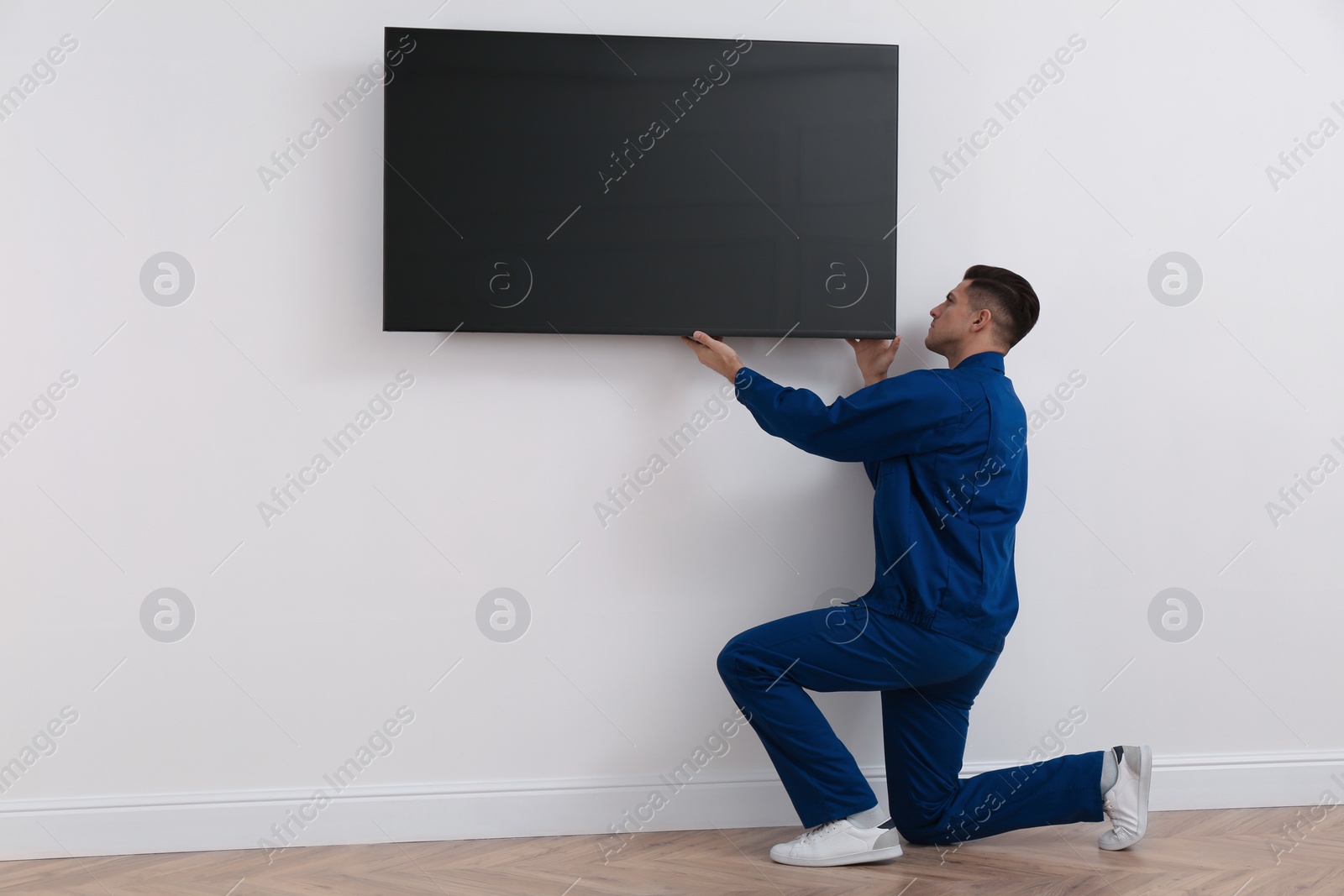 Photo of Professional technician installing modern flat screen TV on wall indoors