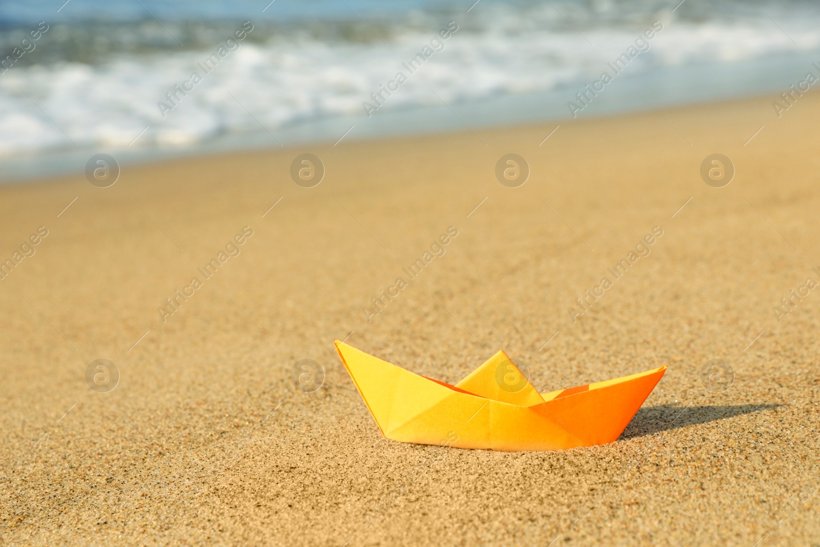 Photo of Orange paper boat on sand near sea, space for text