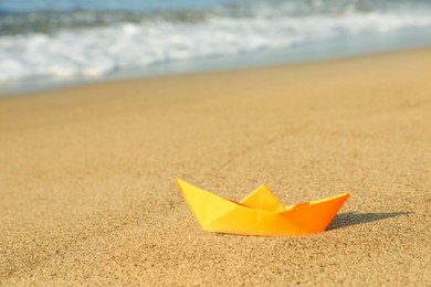 Orange paper boat on sand near sea, space for text