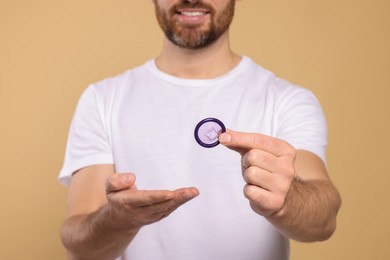 Photo of Man holding condom on beige background, closeup. Safe sex