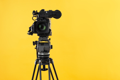 Photo of Modern professional video camera on yellow background. Space for text