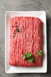 Photo of Raw ground meat, parsley and peppercorns on grey table, top view