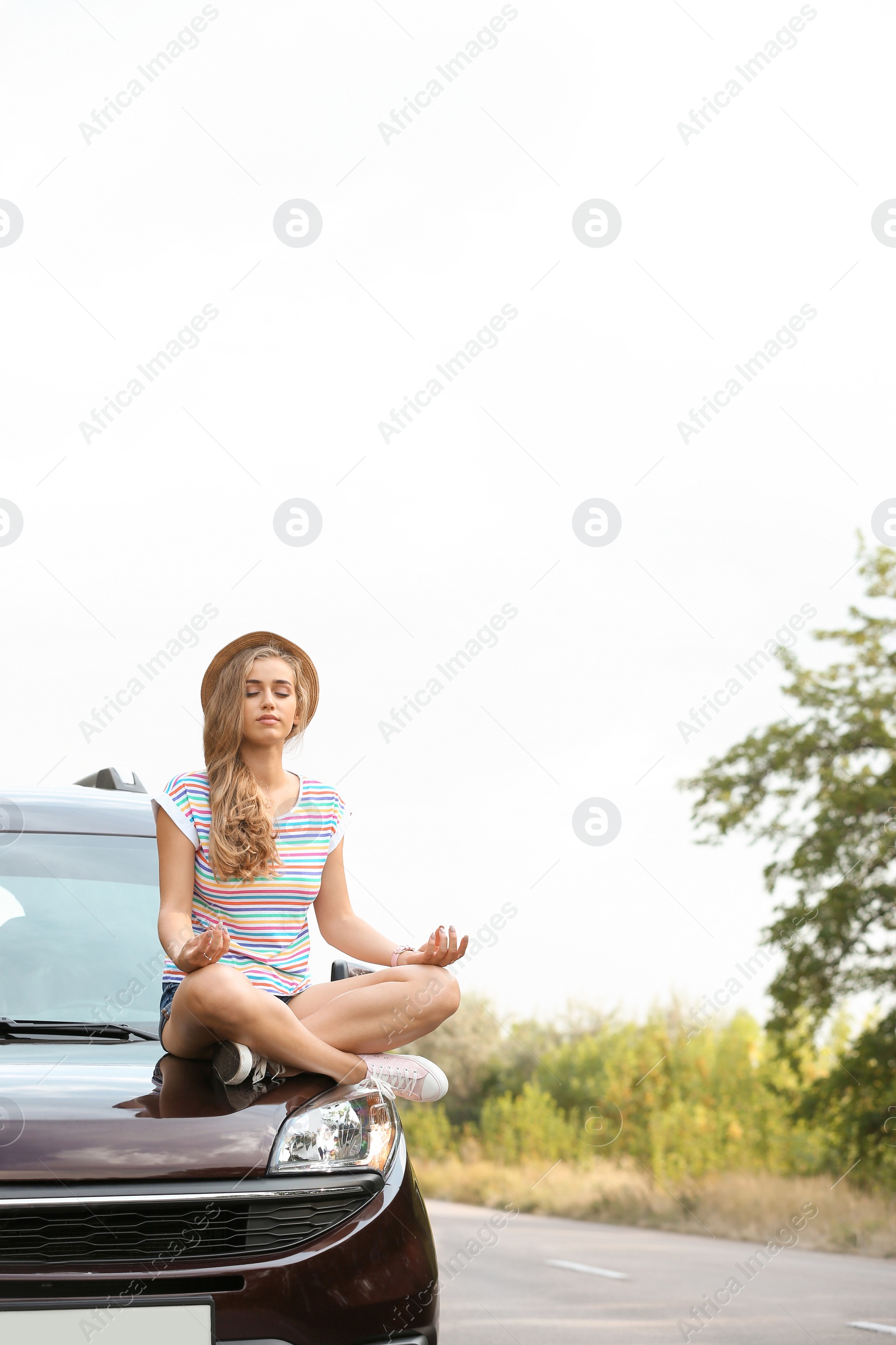 Photo of Young woman meditating on car hood outdoors. Joy in moment