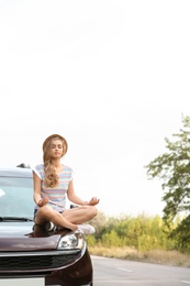 Photo of Young woman meditating on car hood outdoors. Joy in moment