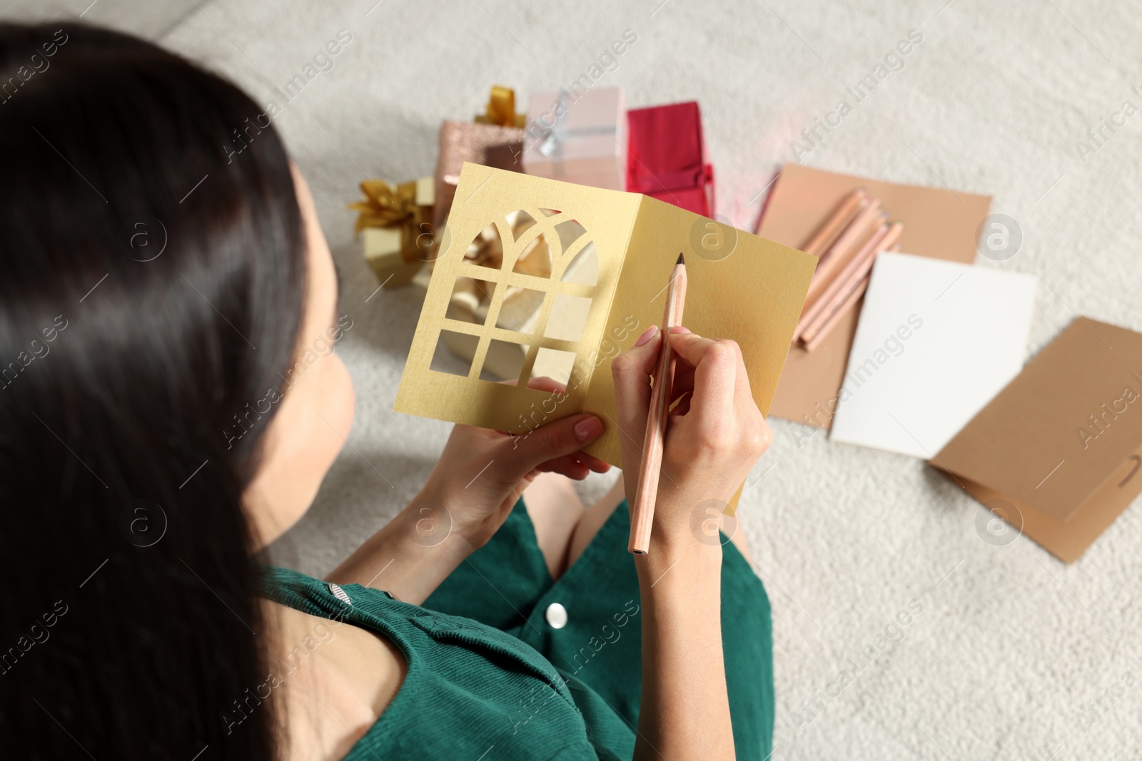 Photo of Woman writing message in greeting card on floor in living room, closeup